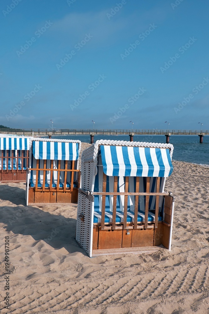 Fototapeta premium Strandkorb on Rugen beach with blue striped canopy and wooden frame by Baltic Sea pier