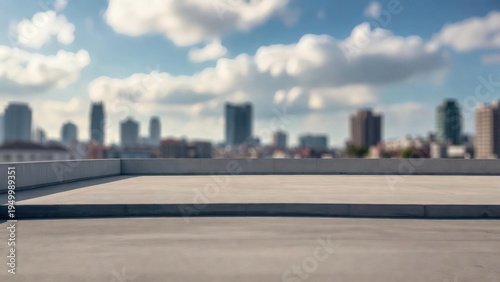 Concrete rooftop overlooks distant city skyline. Blue sky, fluffy clouds frame urban skyline. Smooth surface, low walls frame expansive view. Ideal backdrop for product display or business concept