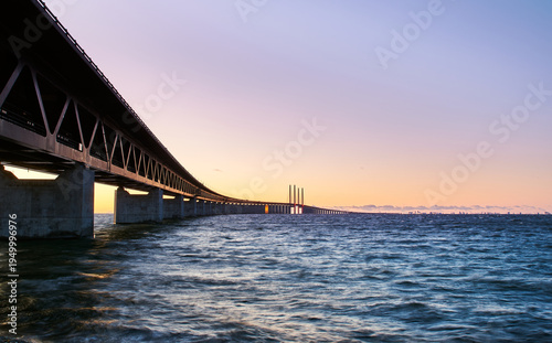 Sunset over Öresund Bridge connecting Malmo, Sweden to Copenhagen, Denmark stretching into the distance above rippling sea with a warm sky. Cross border, modern Scandinavian infrastructure concept
