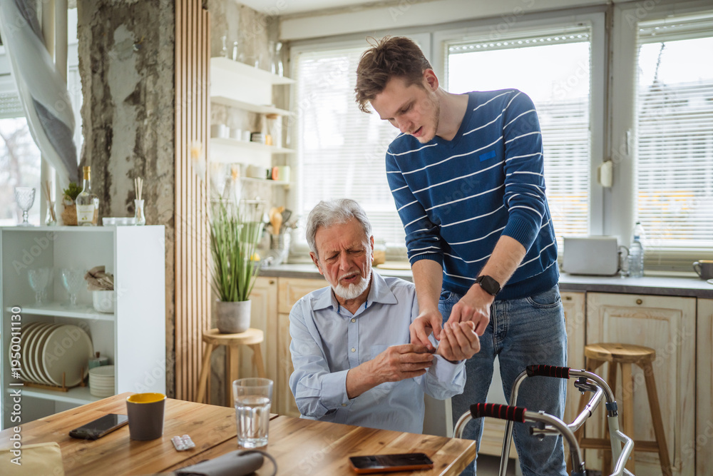 Fototapeta premium Young man assisting senior at home with health monitor