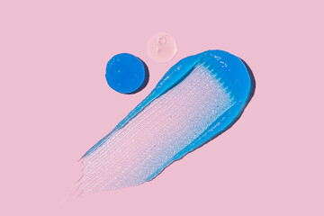 Swatch of blue exfoliant and serum on pink background with copy space
