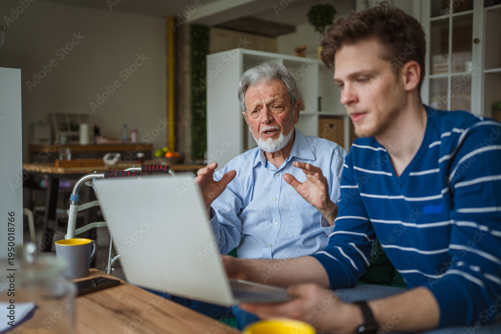 Fototapeta premium Young man teaching senior man using laptop at home