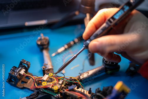 Foto Technician soldering a 5-inch FPV drone on a workbench, with exposed electronics, wires, and repair tools