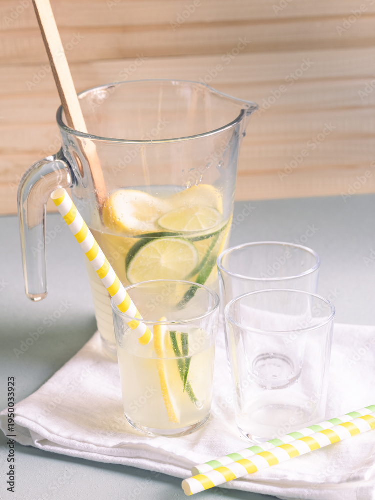 Fototapeta premium a pitcher and glasses with lemonade and lime and lemon slices on a beige linen tablecloth in natural light