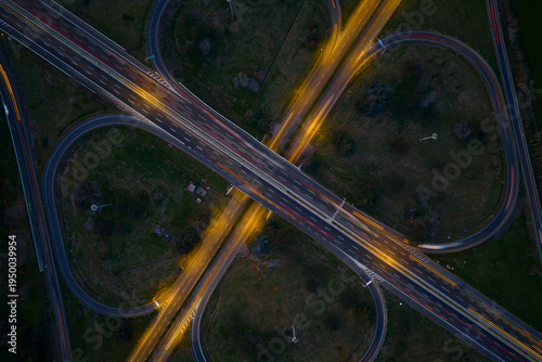 Aerial view of the cloverleaf interchange glows with golden trails of light against the dark green landscape, Rome, Lazio, Italy.