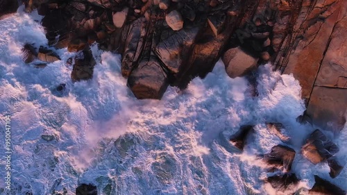 Aerial view of the foamy, white-crested waves crashing against the jagged, dark rocks along the coastline, Cape Town, Western Cape, South Africa.