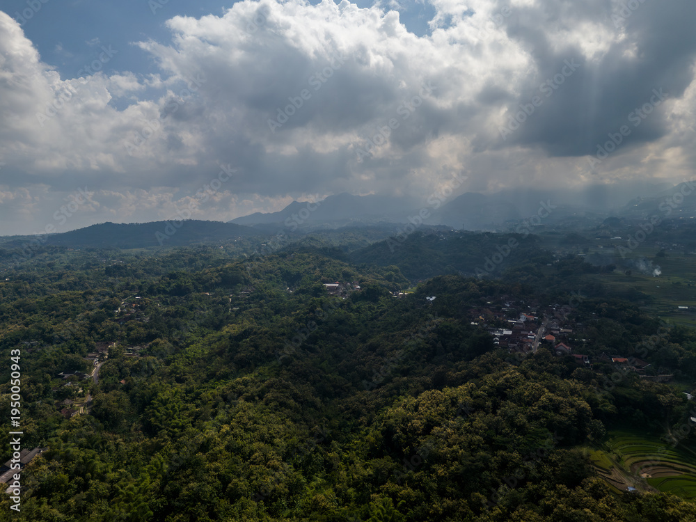 Fototapeta premium Dramatic sun rays breaking through clouds over the misty valley of Mount Lawu slopes.