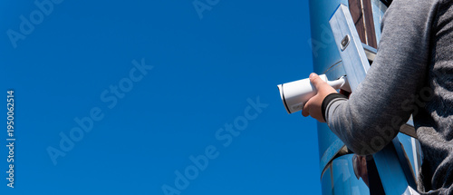 Tableau sur toile Worker installs a security camera on a tall pole under a clear blue sky