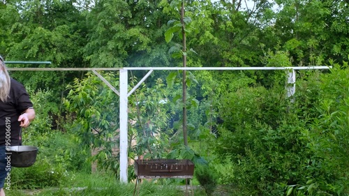 Senior bearded man lifting a heavy cauldron with ready soup from the grill in a lush summer garden.