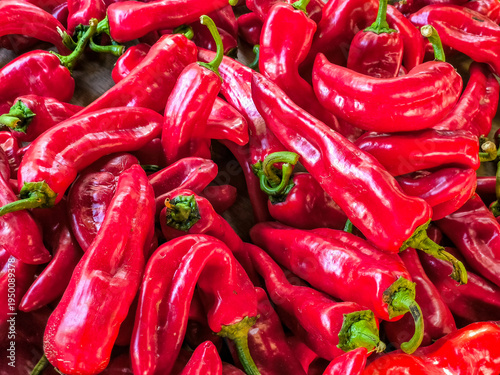 Vibrant red chili peppers with green stems piled on wooden surface, elongated curved shapes and glossy skins creating a spicy full-frame texture for Mexican cuisine and market scenes.