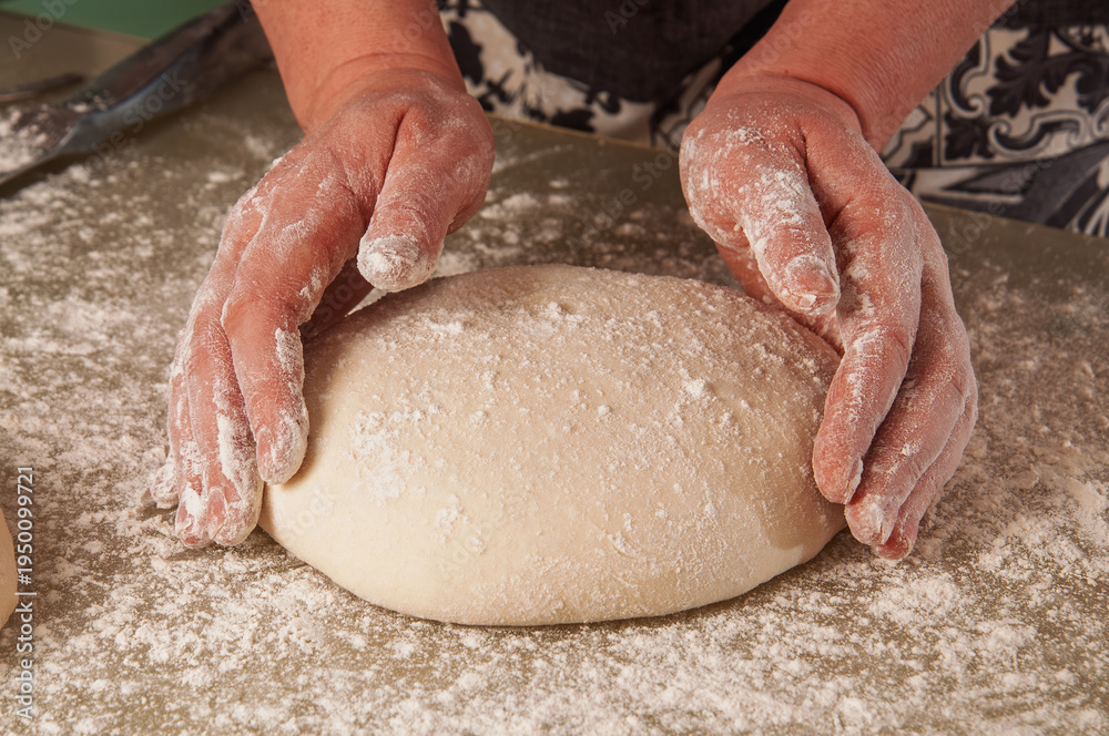 Fototapeta premium Hands shaping raw dough covered in flour on a floured surface, preparing for baking