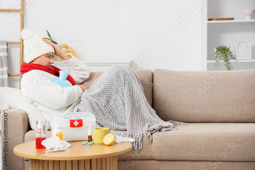 Canvas Print Sick mature woman with medicine and hot water bottle lying on sofa at home