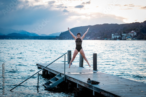 Quadro em tela Woman jumping joyfully on lakeside dock at sunset, cold water plus 8 degree