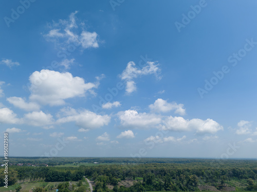 High angle perspective of vast blue sky and fluffy clouds over tropical teak forest landscape.