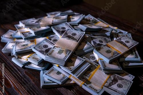 Large stack of one hundred dollar bills arranged on a wooden surface in a well-lit room during the day