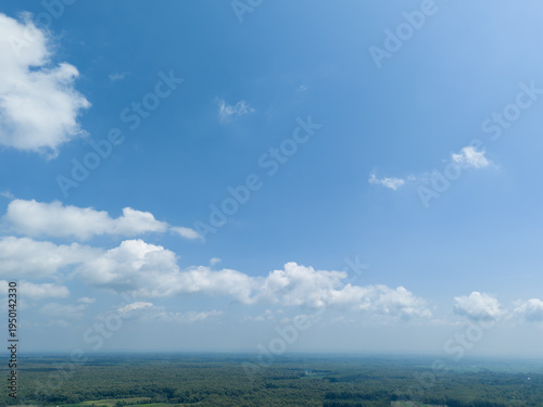 High angle perspective of vast blue sky and fluffy clouds over tropical teak forest landscape.