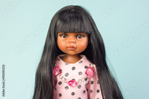Realistic vinyl toy doll with beautiful dark hair and dark skin in stylish clothes on a blue background, close-up portrait