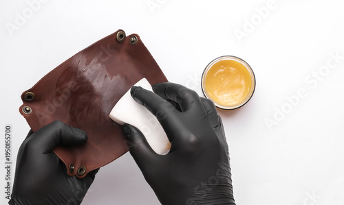 Fotografie Tanner applies cream to a leather organizer on white background