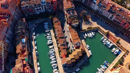 High angle view of residential marina with moored yachts. Aerial shot of Mediterranean town houses surrounding a basin filled with private boats and parked cars.