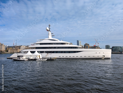 Luxury Superyacht Docked on Urban Riverfront Marina. Massive modern vessel moored beside floating pontoon and temporary tents along a metropolitan waterfront, showcasing sleek naval architecture, mult