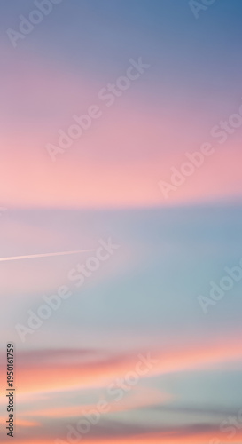 Soft pastel gradient sunset sky displays horizontal layers of pink, blue, and orange hues above a faint contrail.