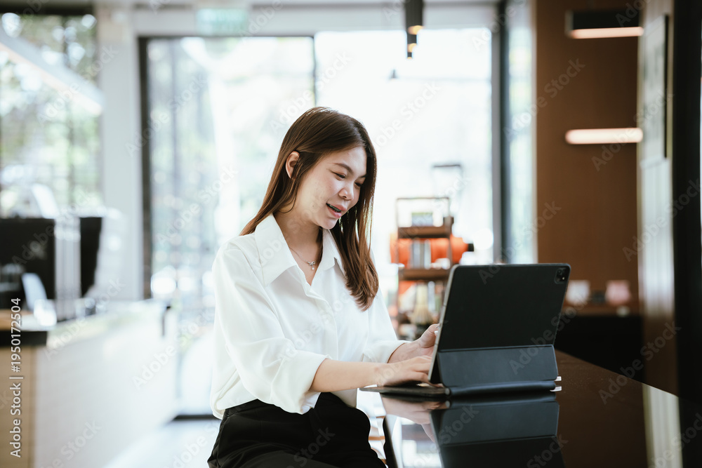 Obraz premium A young woman using a smartphone while holding a credit card, sitting at a table with a tablet in a modern cafe, representing mobile payment and online shopping lifestyle.
