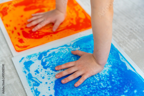 Child hands pressing colorful sensory gel mats creating moving patterns during tactile play. Sensory stimulation and occupational therapy concept for autism support and sensory integration development