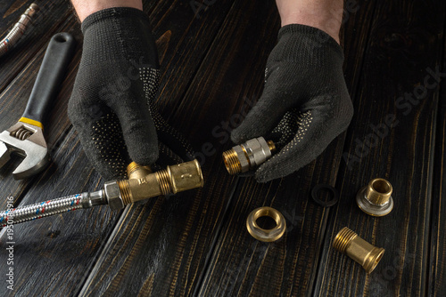 Experienced plumber connects brass fittings to gas hose. Hands of master in work gloves while working in workshop on black table