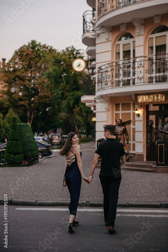 Fotografía Happy young stylish couple holding hands and walking across a crosswalk near a b