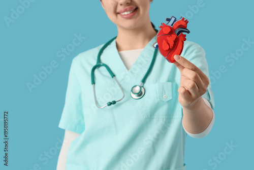 Female doctor with paper heart on blue background, closeup. World Health Day