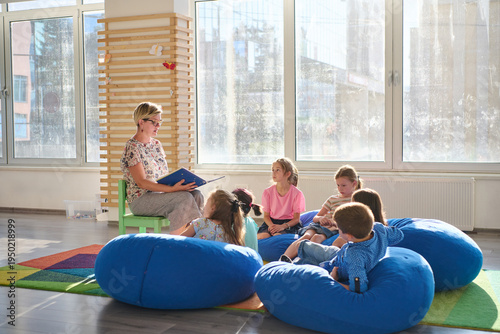 Teacher reading a picture book to young children during cozy classroom circle time on bean bags