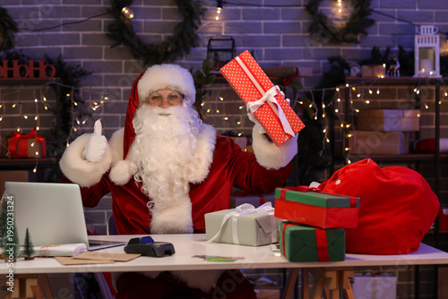 Santa Claus with Christmas gift boxes and laptop showing thumb-up in post office