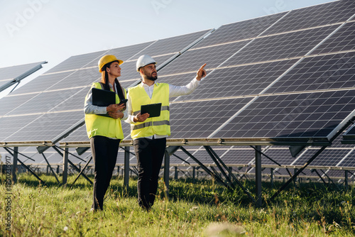 Wallpaper Mural Explaining the plan and showing are to the woman. Two solar engineers standing together at a photovoltaic field, in bright safety vests Torontodigital.ca