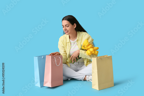 Beautiful young happy woman with tulip flowers and shopping bags sitting on b...