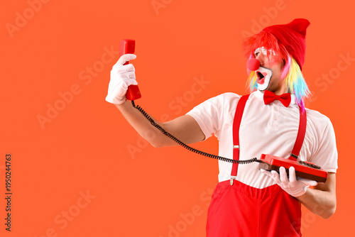Portrait of surprised clown with retro telephone on orange background. April ...