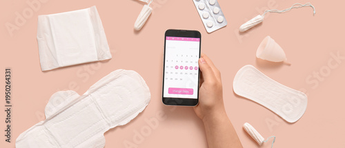 Fotografie Female hand with menstrual calendar on screen of mobile phone and feminine hygie