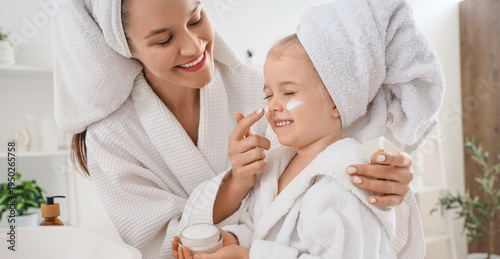 Cuadro en lienzo Cute little happy girl and her mother in bathrobes applying cream at home