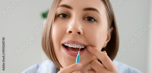 Tableau sur toile Young woman with dental braces cleaning teeth in bathroom, closeup