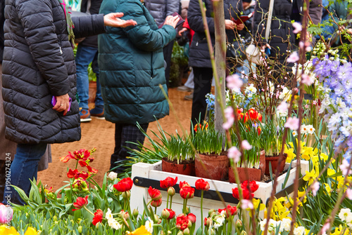 Фотография Group of people in winter jackets admiring colorful flowers in pots at a garden