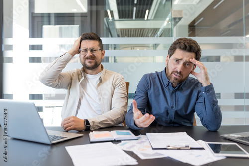 Εκτύπωση καμβά Two stressed businessmen in a modern office looking perplexed and frustrated whi