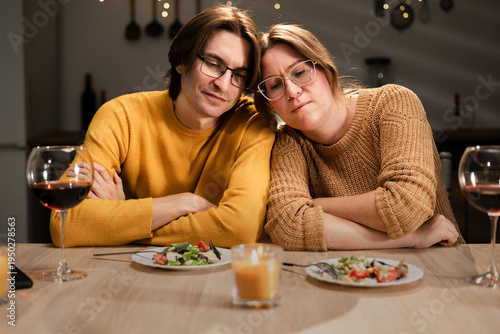 Tired burnt out couple in love sitting head to head at table having dinner at home in evening