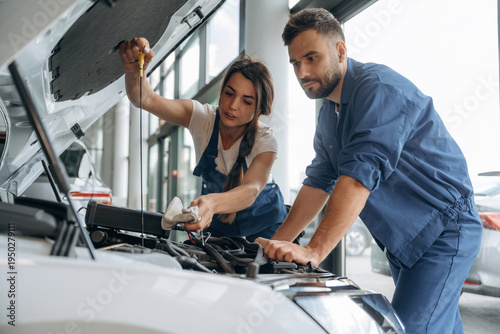 Hood is opened, checking the state of car. Auto repair shop employees are working together. Man and woman