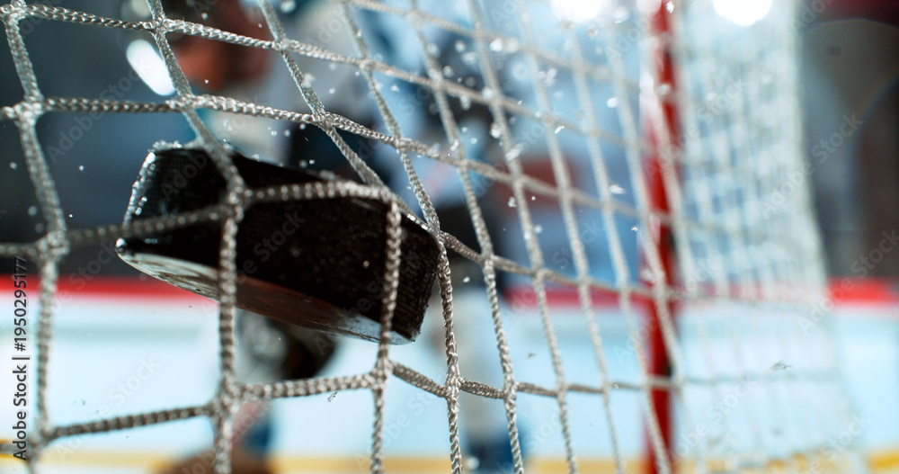 Fototapeta premium Close-up action shot of an ice hockey puck hitting the goal net during a scoring moment. Dynamic sports scene with ice spray and a blurred hockey player in the background.