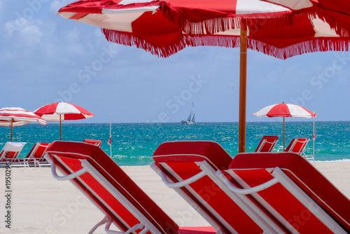 Εκτύπωση καμβά A stunning sunny beach with colorful loungers and umberellas and turquoise blue sea and a Sailing yacht in the distance