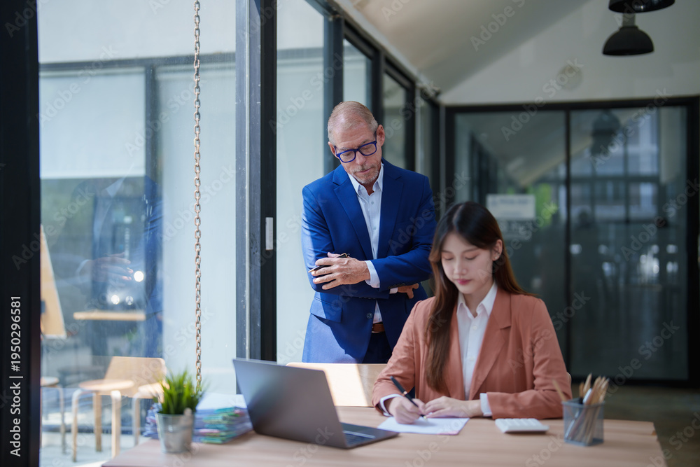 Fototapeta premium Manager supervising female employee writing notes in modern office