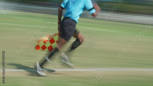 Assistant referee captured mid stride running swiftly along sidelines with fluorescent shirt waving flag signaling call for players during match
