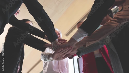 Diverse group of business professionals placing hands together in team unity gesture during meeting in modern office.