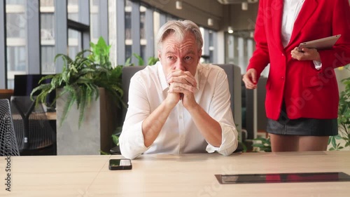 Young businesswoman encouraging senior colleague during discussion at office desk, showing teamwork, leadership support, and professional workplace collaboration.