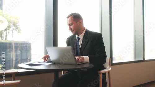 Professional businessman speaking on smartphone while holding financial report near office window during work discussion.