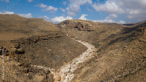 Desert canyon valley with dry riverbed under cloudy sky